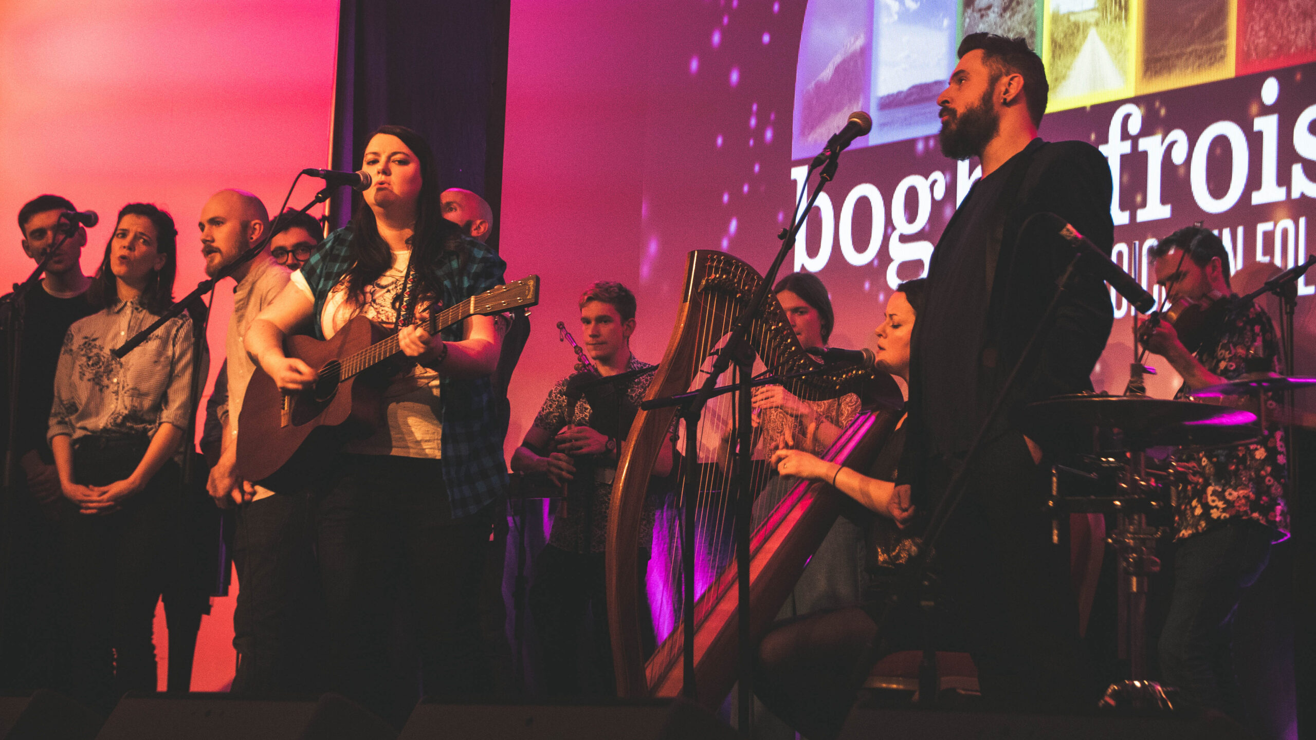 A picture of performers at the DGArts Fest. They play instruments onstage before a rosy pink background.